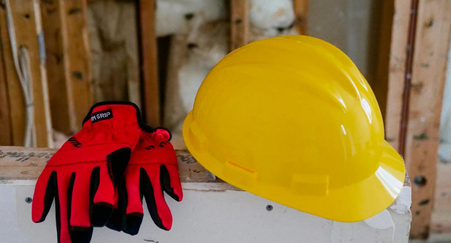 Close-up of a yellow hard hat and red gloves on a construction site, symbolizing safety and work.